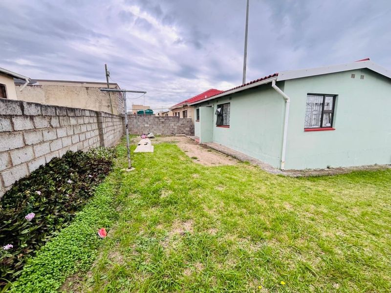 Rear view of the property featuring a grassed garden area, concrete block boundary walls, and exterior building facade with metal window frames.