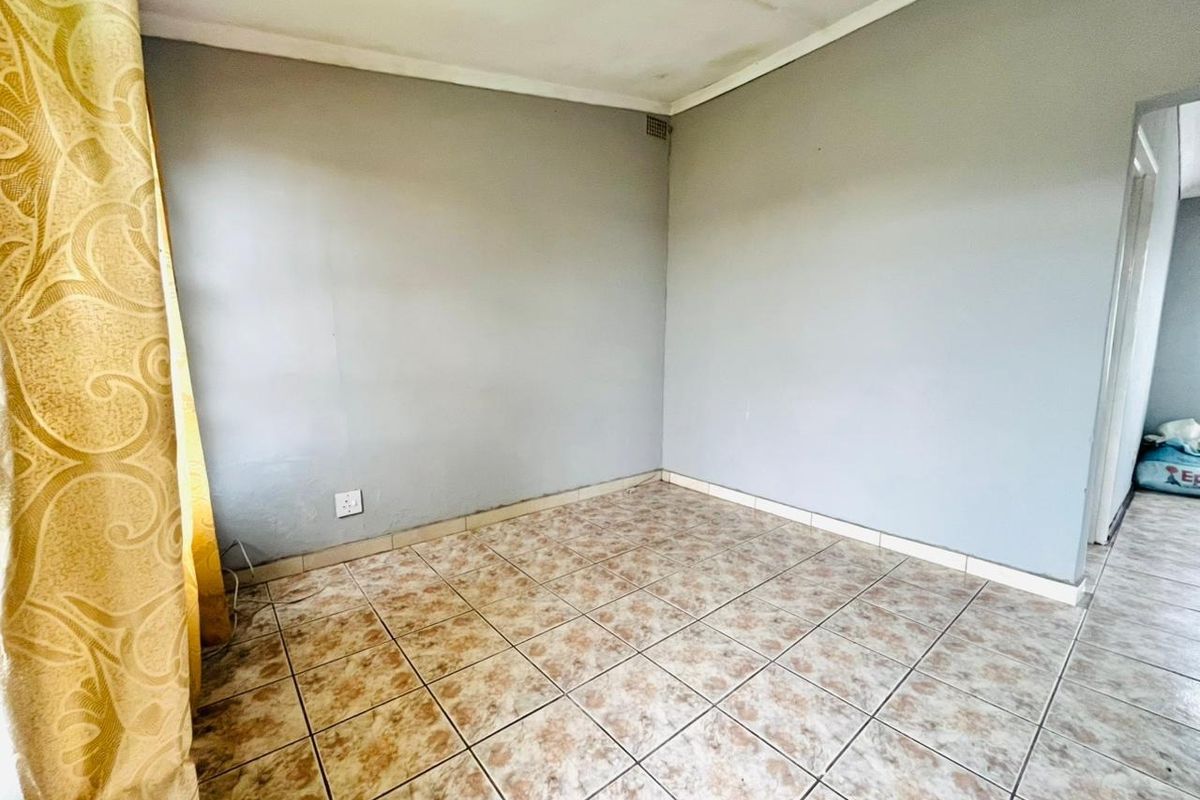 An empty bedroom featuring tiled flooring, neutral grey walls, and standard ceiling cornicing, offering a blank canvas for potential interior updates.