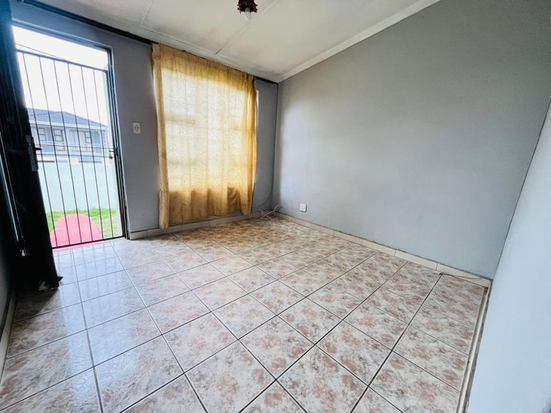 An empty living room featuring tiled flooring, a security gate, and direct access to the exterior, offering a blank canvas for renovation.