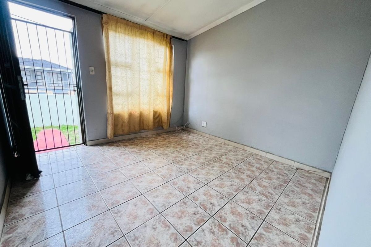 An empty living room featuring tiled flooring, a security gate, and direct access to the exterior, offering a blank canvas for renovation.