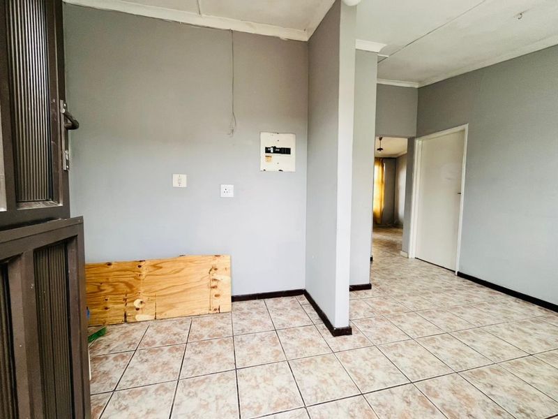 An empty hallway featuring ceramic tiled flooring, neutral grey walls, and a visible electrical distribution board, leading into an adjacent living space.