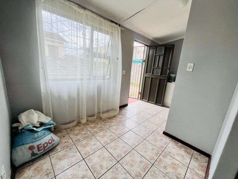 A simple entry area featuring tiled flooring, a security gate, and window security bars, providing direct access to the exterior.