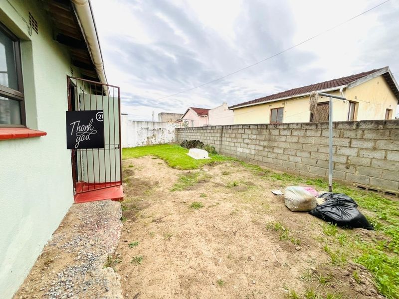 A rear exterior view of the property featuring a concrete block boundary wall, a metal security gate, and a basic garden area.