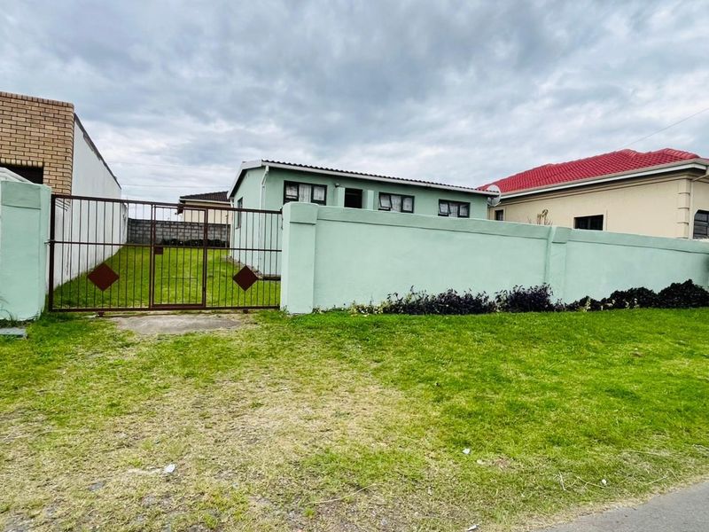 A view of the property's front exterior, featuring a perimeter wall, metal gate, and a grassed yard area.