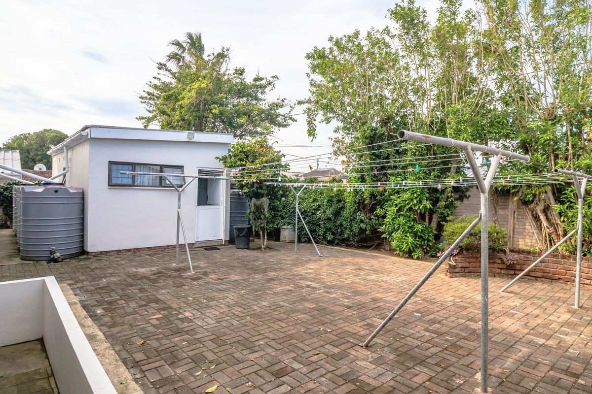 A paved rear courtyard featuring a detached outbuilding, water storage tanks, and a functional metal washing line area enclosed by brick boundary walls.