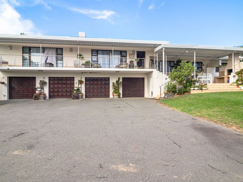 Spacious multi-level home featuring a four-car garage, an expansive upper balcony with stainless steel railings, and a covered patio area with a built-in braai.