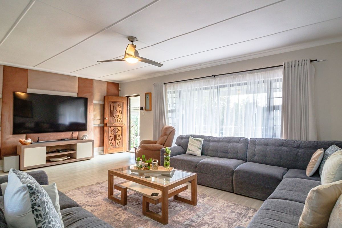 Spacious living room featuring tiled flooring, a ceiling fan, and decorative wall paneling, with direct access to the exterior through a sliding glass door.