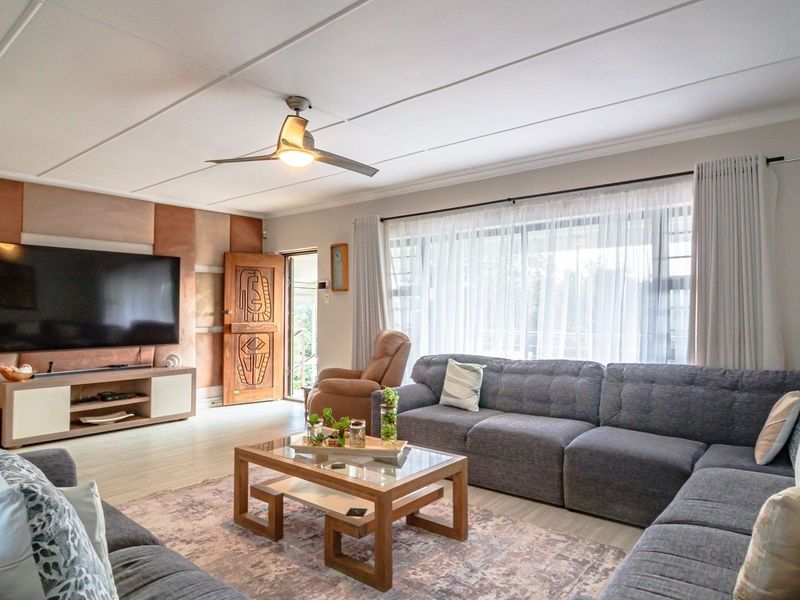 Spacious living room featuring tiled flooring, a ceiling fan, and decorative wall paneling, with direct access to the exterior through a sliding glass door.