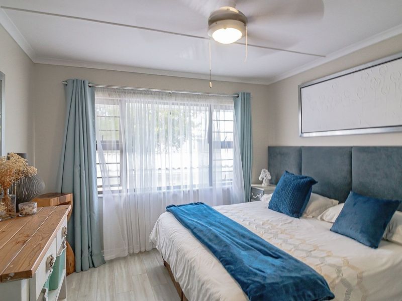 A well-maintained bedroom featuring laminate flooring, a ceiling fan, and window security bars, offering a comfortable and functional living space.
