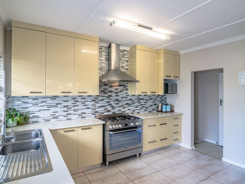 A well-maintained kitchen featuring light-toned cabinetry, a stainless steel gas stove with extractor fan, mosaic backsplash, and tiled flooring.