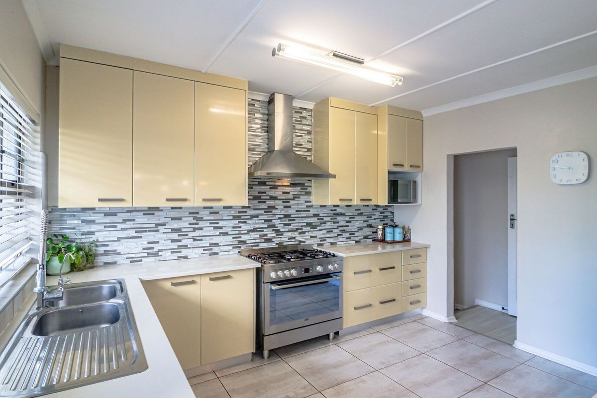 A well-maintained kitchen featuring light-toned cabinetry, a stainless steel gas stove with extractor fan, mosaic backsplash, and tiled flooring.
