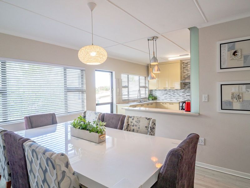 Open plan dining area featuring laminate flooring and pendant lighting, seamlessly connected to a functional kitchen with tiled backsplash and modern cabinetry.