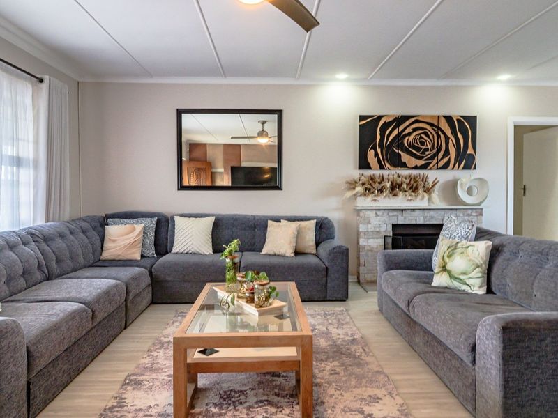 A well-maintained living room featuring a stone fireplace, ceiling fan, and light-toned laminate flooring, creating a comfortable and inviting atmosphere.