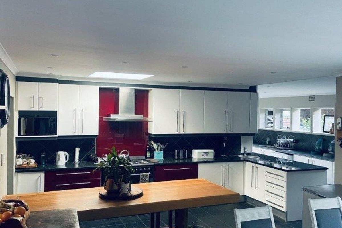 Spacious kitchen featuring modern two-tone cabinetry, a red glass splashback, integrated appliances, and a large central island with a wooden countertop.