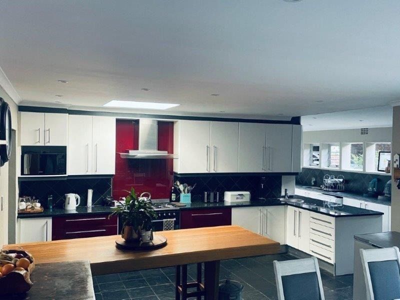 Spacious kitchen featuring modern two-tone cabinetry, a red glass splashback, integrated appliances, and a large central island with a wooden countertop.