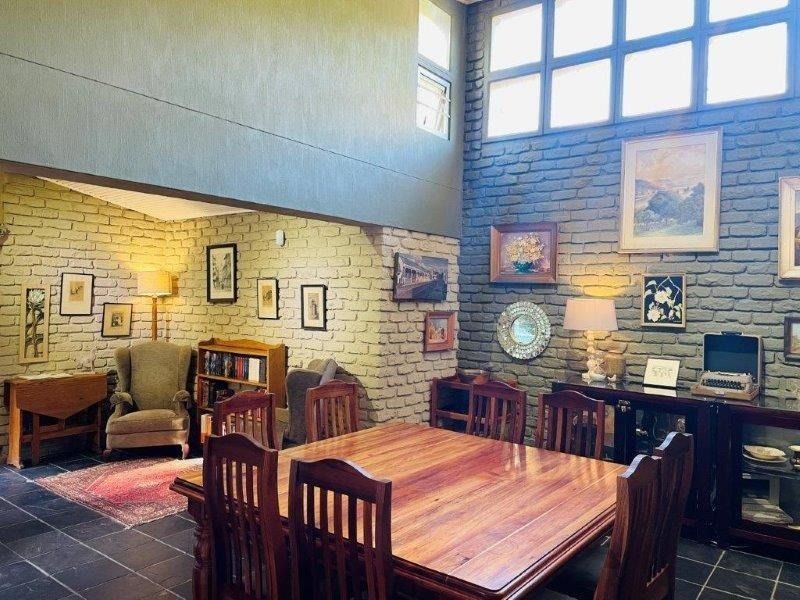 Spacious dining area featuring double-volume ceilings, exposed brick walls, large clerestory windows for natural light, and durable slate tile flooring.
