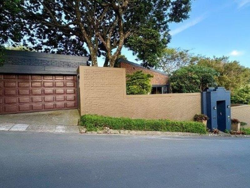 Front exterior view of the property featuring a secure boundary wall, pedestrian entrance, and a garage with a paneled door.