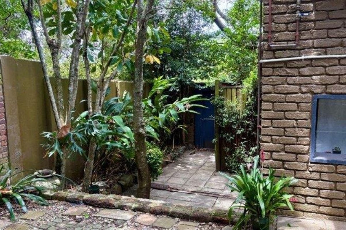 A private rear garden area featuring a paved walkway, established trees, and brick boundary walls, providing a secluded outdoor space.