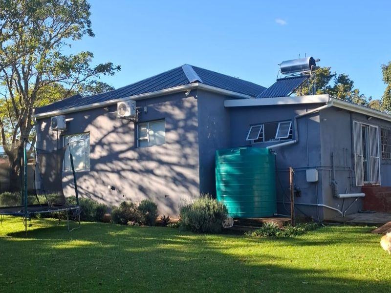 Rear view of the house featuring a solar water heating system, water storage tank, and established garden area.