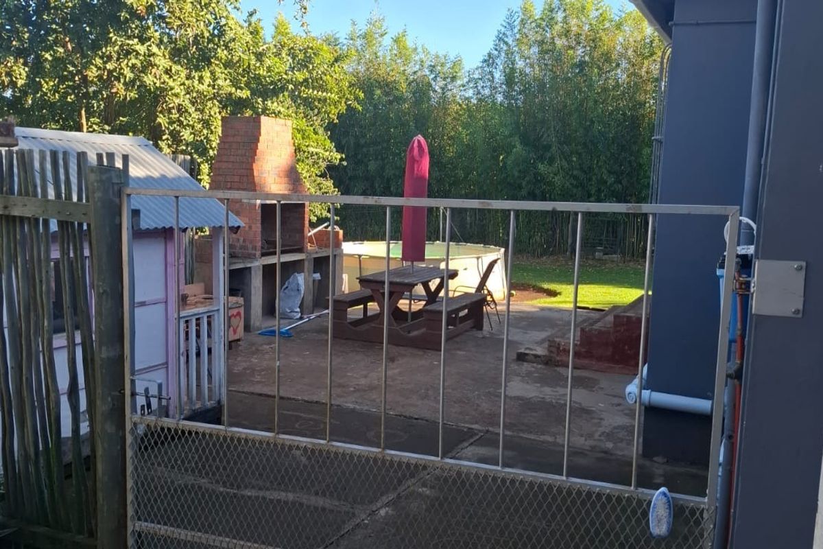 Rear outdoor area featuring a built-in brick braai, concrete patio space, and direct access to the garden and pool area.