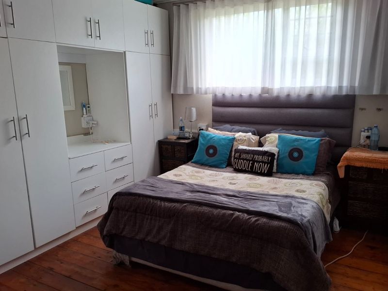 A well-maintained bedroom featuring extensive built-in white cabinetry with an integrated vanity, warm timber flooring, and a modern upholstered headboard.