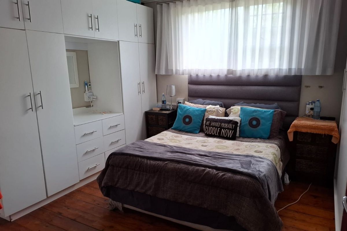 A well-maintained bedroom featuring extensive built-in white cabinetry with an integrated vanity, warm timber flooring, and a modern upholstered headboard.