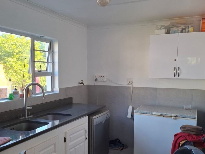 A functional kitchen area featuring a double sink, stone countertops, tiled splashbacks, and white wall-mounted cabinetry with natural light from the window.