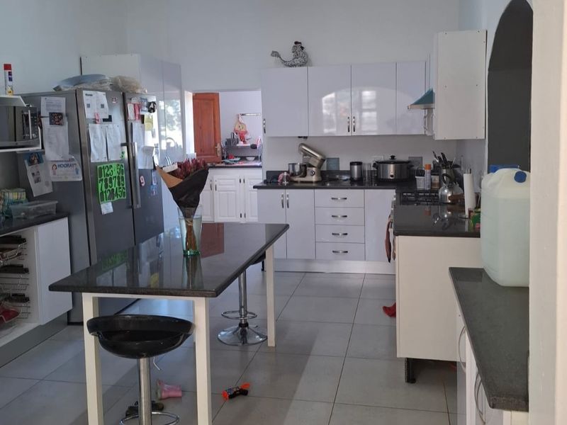 A functional kitchen featuring white gloss cabinetry, granite countertops, a central island, and tiled flooring, with an adjacent scullery area visible.
