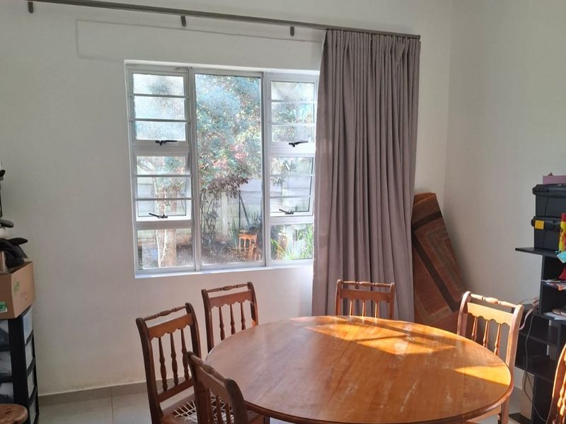 A dining area featuring tiled flooring and large aluminium-framed windows that provide natural light and a view of the garden.