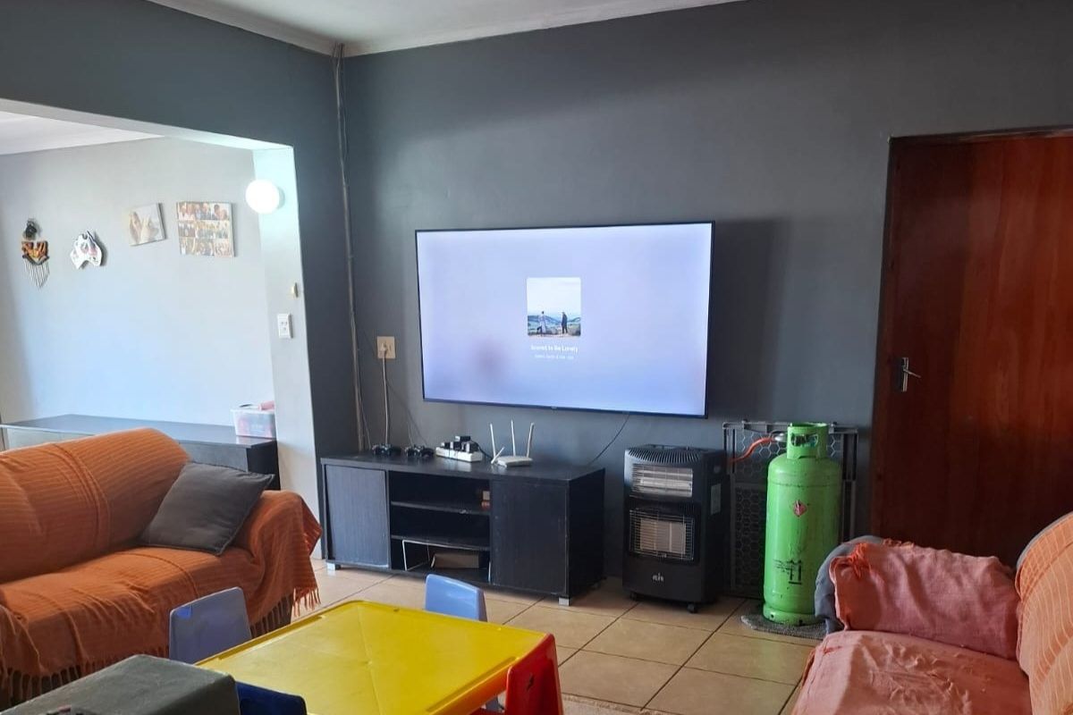 A living room featuring tiled flooring and a wall-mounted television, with an open-plan layout connecting to adjacent living spaces.