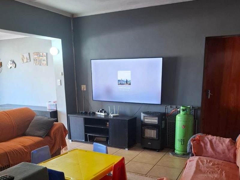 A living room featuring tiled flooring and a wall-mounted television, with an open-plan layout connecting to adjacent living spaces.