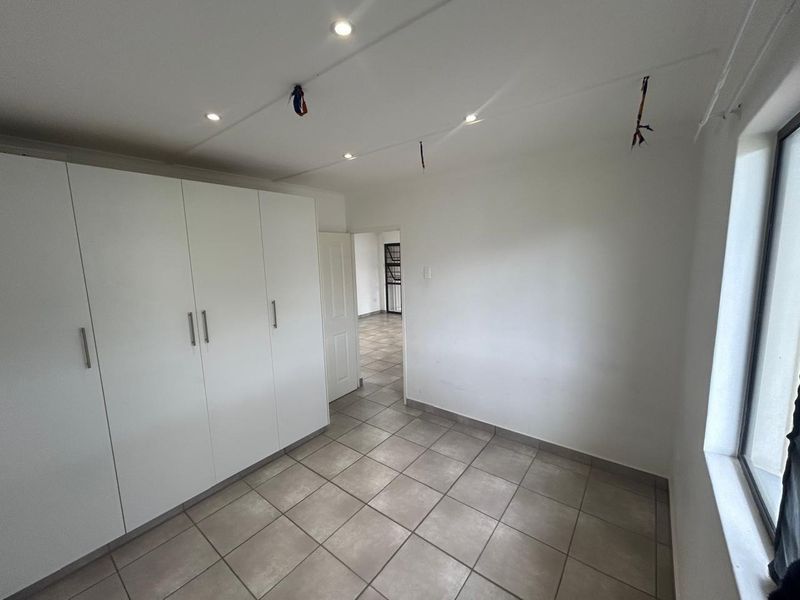 A vacant bedroom featuring built-in cupboards, tiled flooring, and recessed downlighting, with exposed wiring visible on the ceiling.