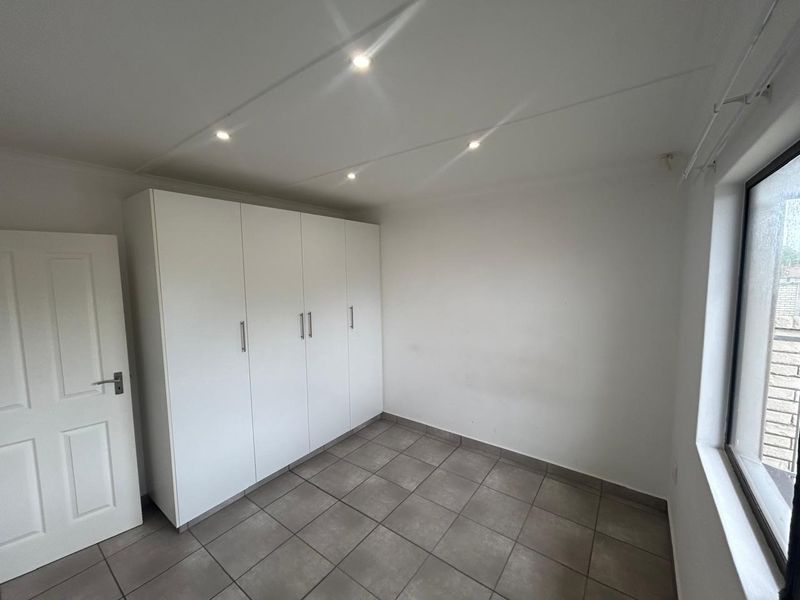 A clean, empty bedroom featuring neutral tiled flooring, built-in white cupboards, and recessed ceiling lighting, offering a versatile space ready for personalization.