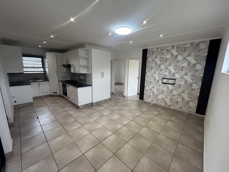 Spacious open-plan living area featuring a modern kitchen with built-in appliances, tiled flooring, and a decorative feature wall in a neutral townhouse setting.