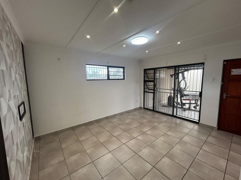 A bright, empty living area featuring neutral tiled flooring, recessed downlighting, a textured feature wall, and a sliding door leading to an outdoor space.
