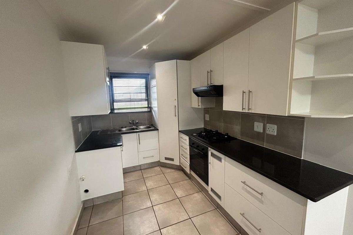 A clean, modern kitchen featuring white cabinetry, black granite countertops, a gas hob, built-in oven, and tiled flooring with a neutral backsplash.