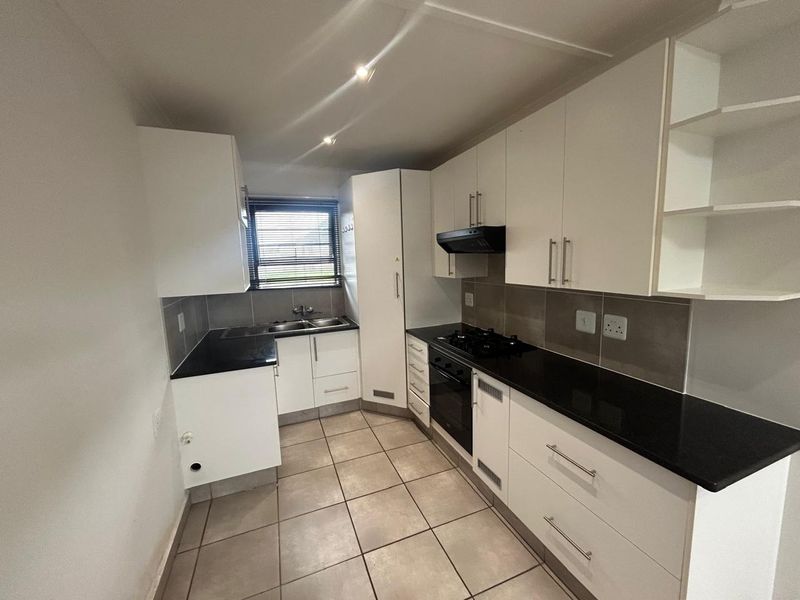 A clean, modern kitchen featuring white cabinetry, black granite countertops, a gas hob, built-in oven, and tiled flooring with a neutral backsplash.