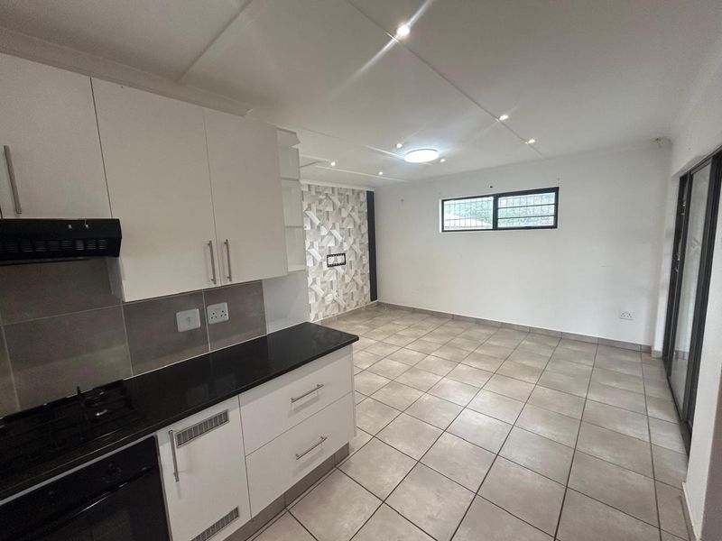 Open-plan kitchen and living area featuring modern white cabinetry, black granite countertops, tiled flooring, and recessed lighting in a clean, vacant space.