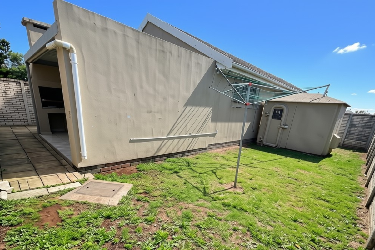 Rear exterior view of the townhouse featuring a paved patio with a built-in braai, a small garden area, and a secure storage unit.