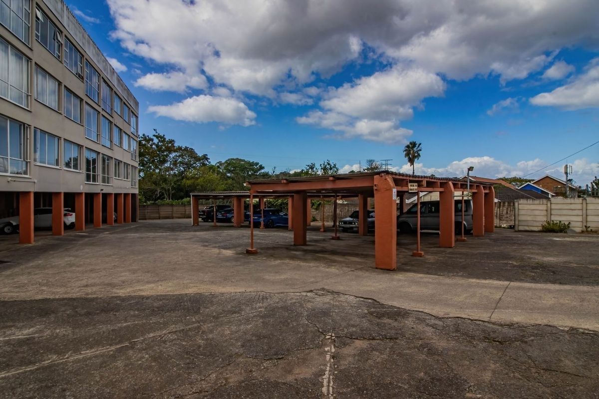 Exterior view of the apartment complex featuring a large concrete parking area with covered bays and multi-story building facade.