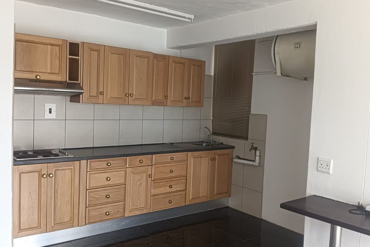 A functional kitchen featuring wooden cabinetry, a tiled backsplash, integrated hob with extractor, and a wall-mounted electric water heater.