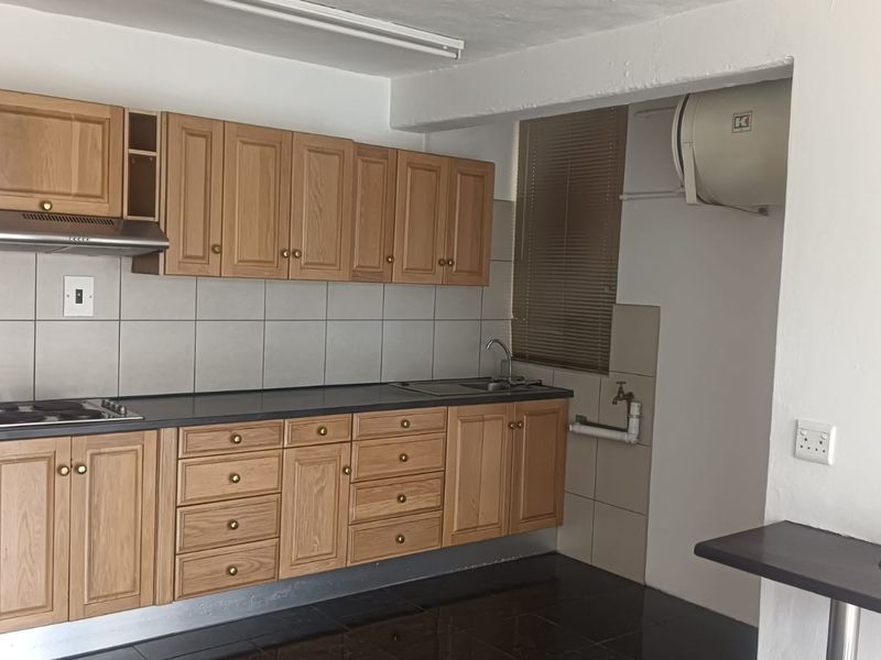 A functional kitchen featuring wooden cabinetry, a tiled backsplash, integrated hob with extractor, and a wall-mounted electric water heater.