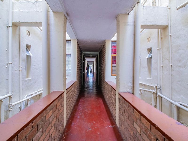 An open-air apartment complex corridor featuring brick balustrades, concrete support columns, and external-facing windows.