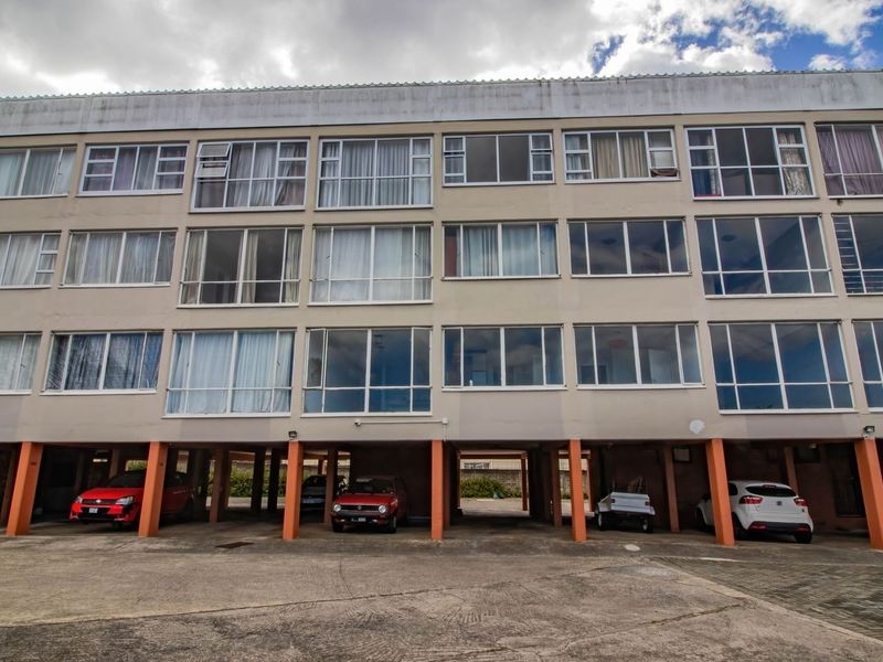 Front elevation of a multi-story apartment building featuring an open-plan ground level parking area and extensive glass window frontage.