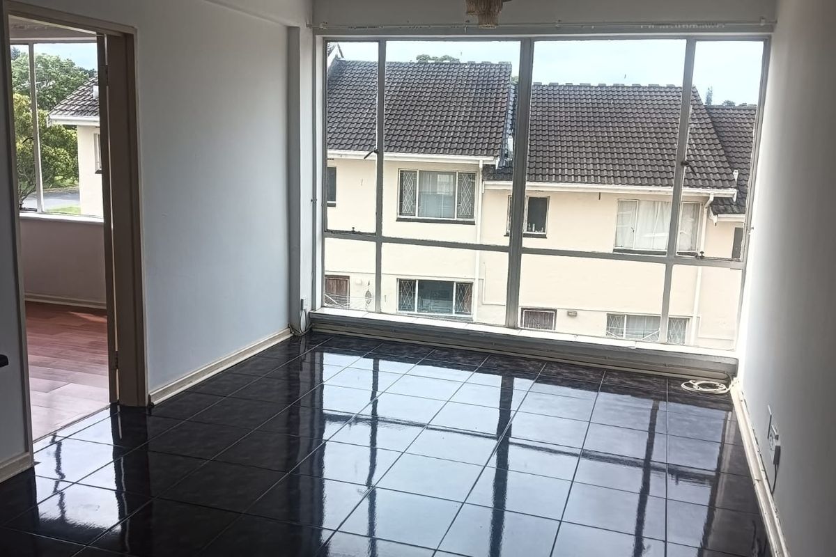 A bright, empty living area featuring dark ceramic floor tiles and large windows that provide ample natural light and a view of the surrounding neighborhood.