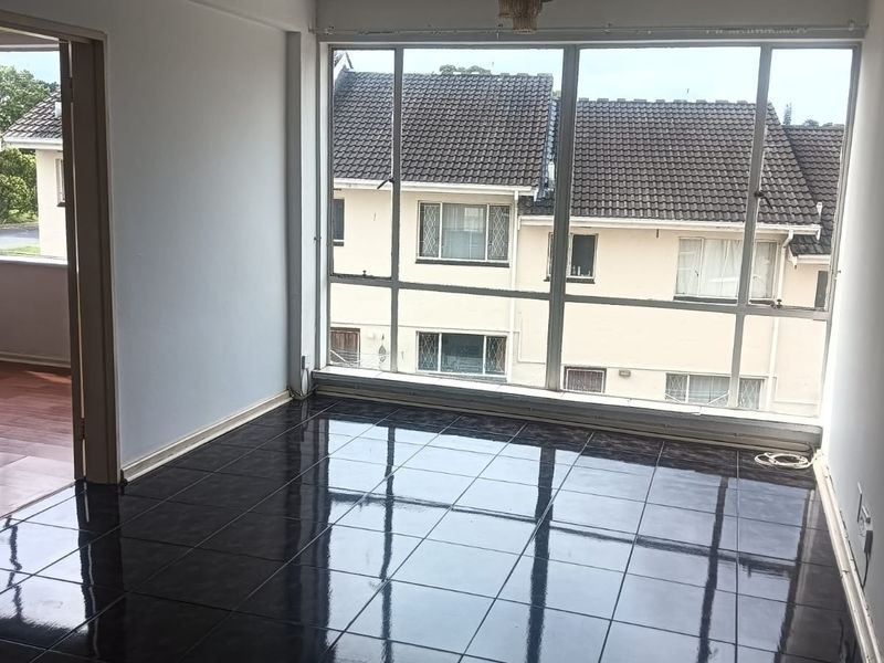 A bright, empty living area featuring dark ceramic floor tiles and large windows that provide ample natural light and a view of the surrounding neighborhood.