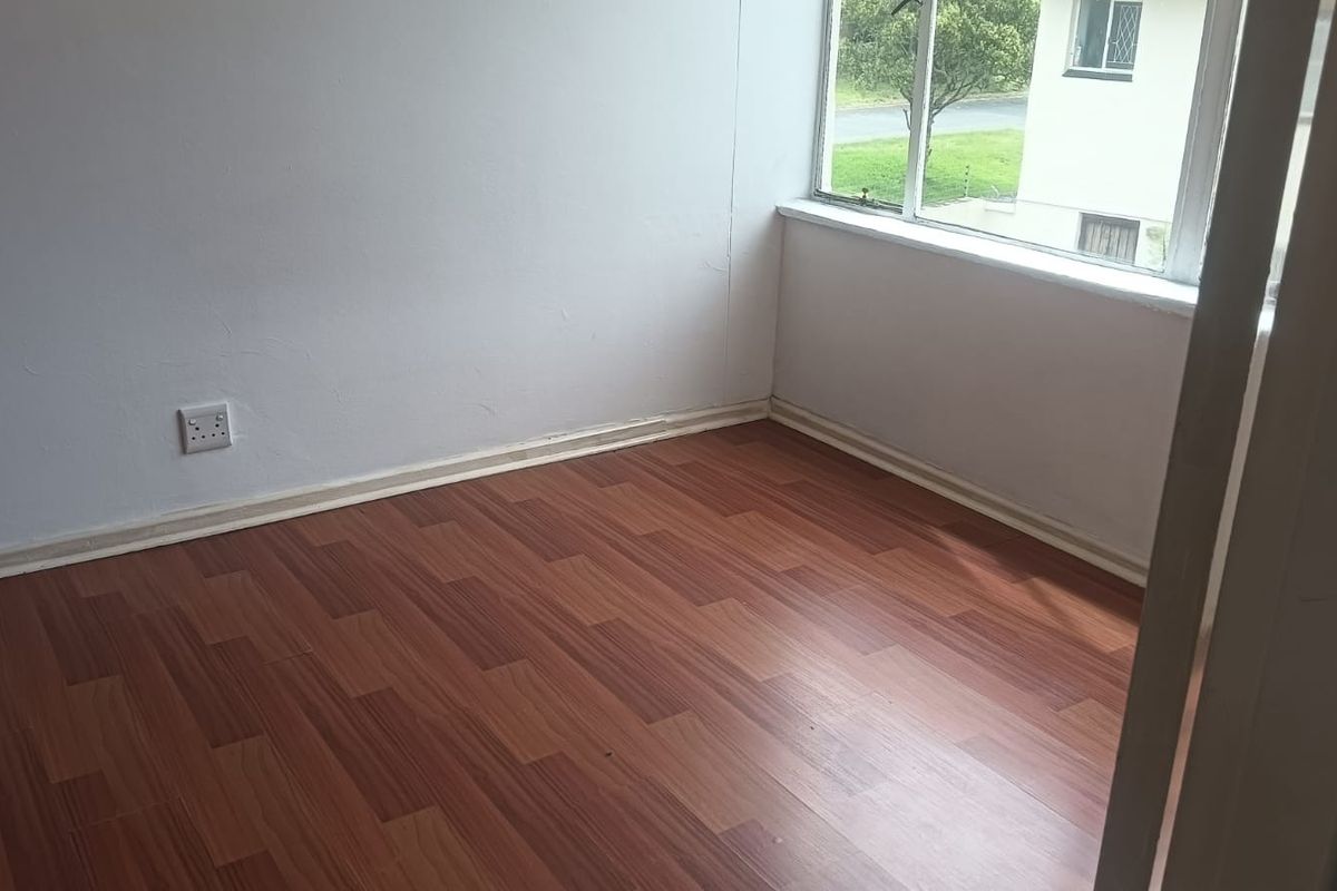 An empty bedroom featuring laminate wood flooring, white walls, and a large window providing natural light.