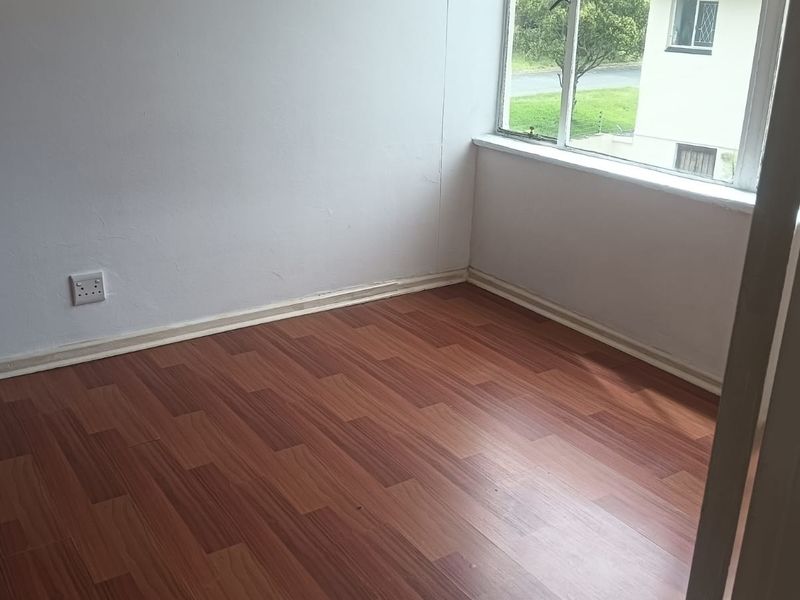 An empty bedroom featuring laminate wood flooring, white walls, and a large window providing natural light.