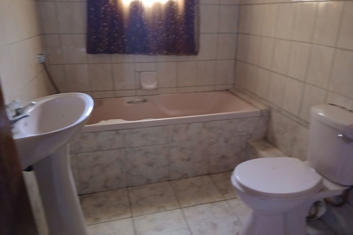 A dated bathroom featuring a pedestal basin, built-in bathtub, and toilet with full-height ceramic wall tiling.