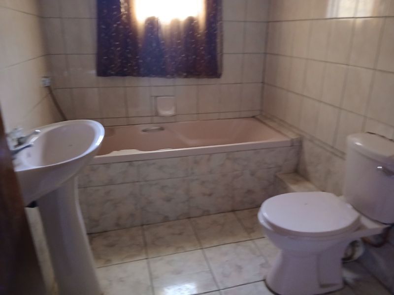 A dated bathroom featuring a pedestal basin, built-in bathtub, and toilet with full-height ceramic wall tiling.
